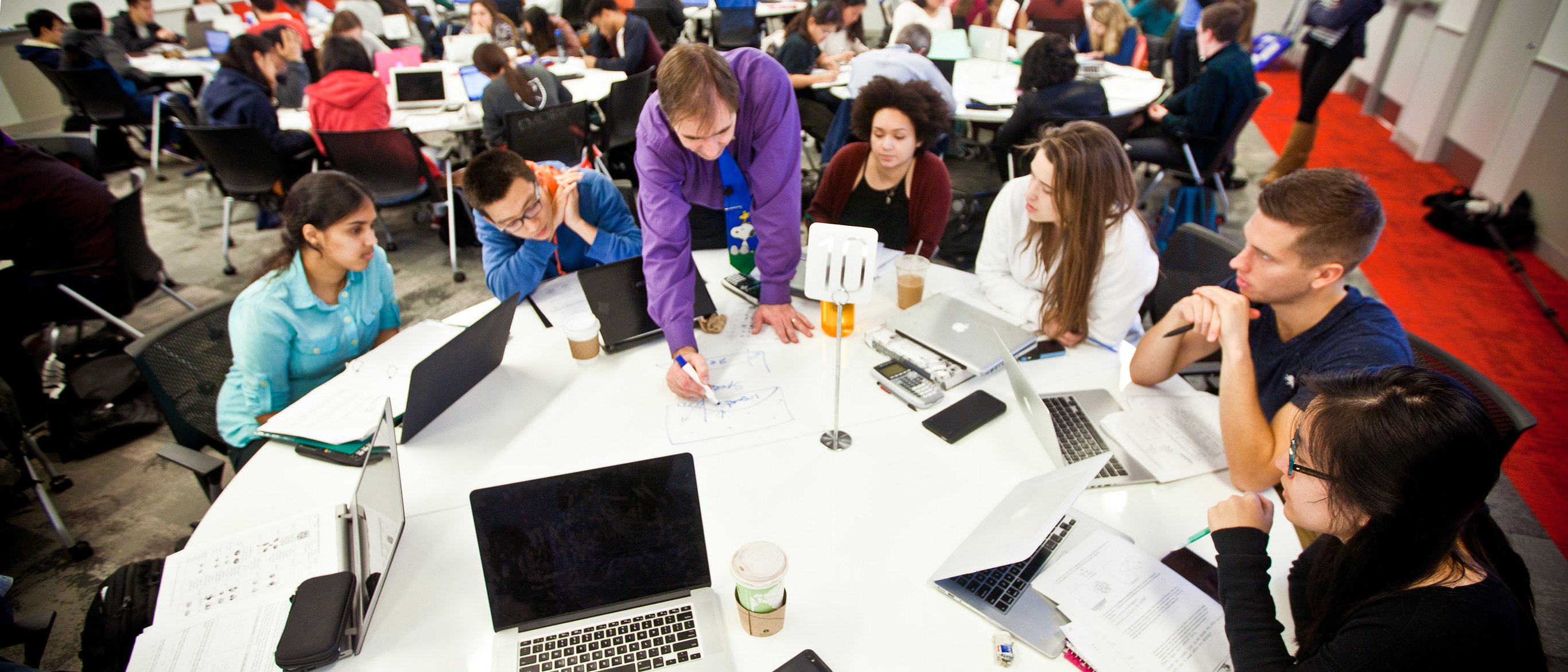Professor wwrtiting on desk with students